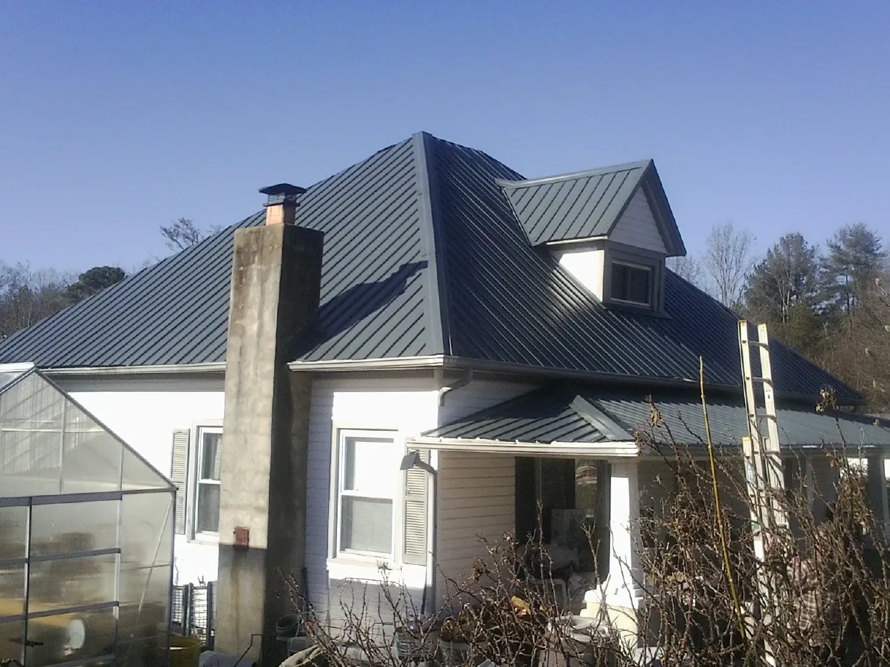Dark blue standing seam metal roof on a white farmhouse with dormer — Slate & Tile Roof Repair by Roofing Brothers in Boxborough