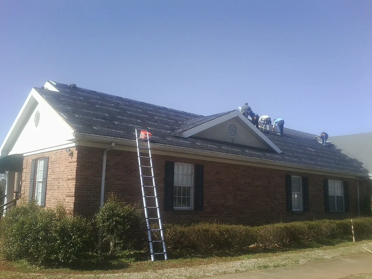 Crew tearing shingles off a brick ranch roof with a ladder set — Metal Roof Repair work by our crew in Boxborough