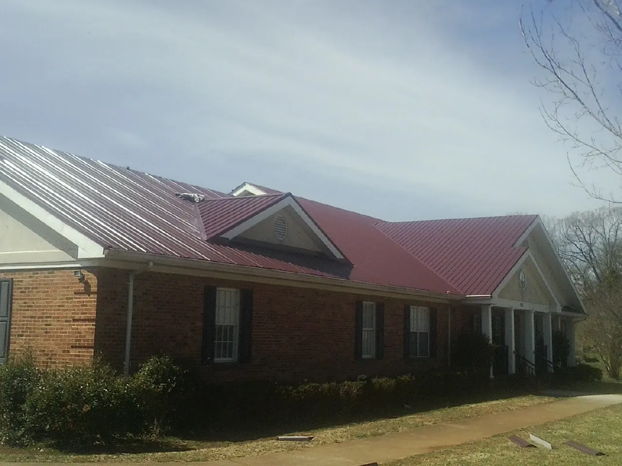 Red metal roof with gabled entries on a long brick building, from a Hail Damage Roof Repair job in Boxborough