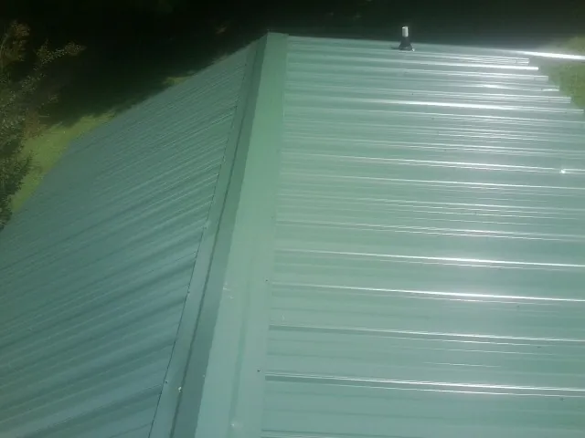 New green metal panels meeting at the ridge of a roof — Flat Roof Repair work by our crew in Boxborough