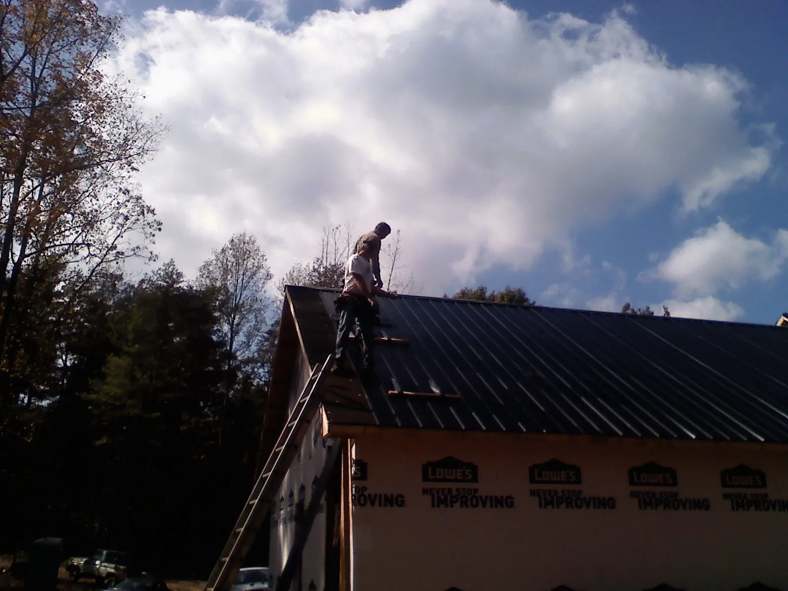 Roofer fastening dark metal panels high against a cloudy sky, from a Roof Inspection job in Boxborough