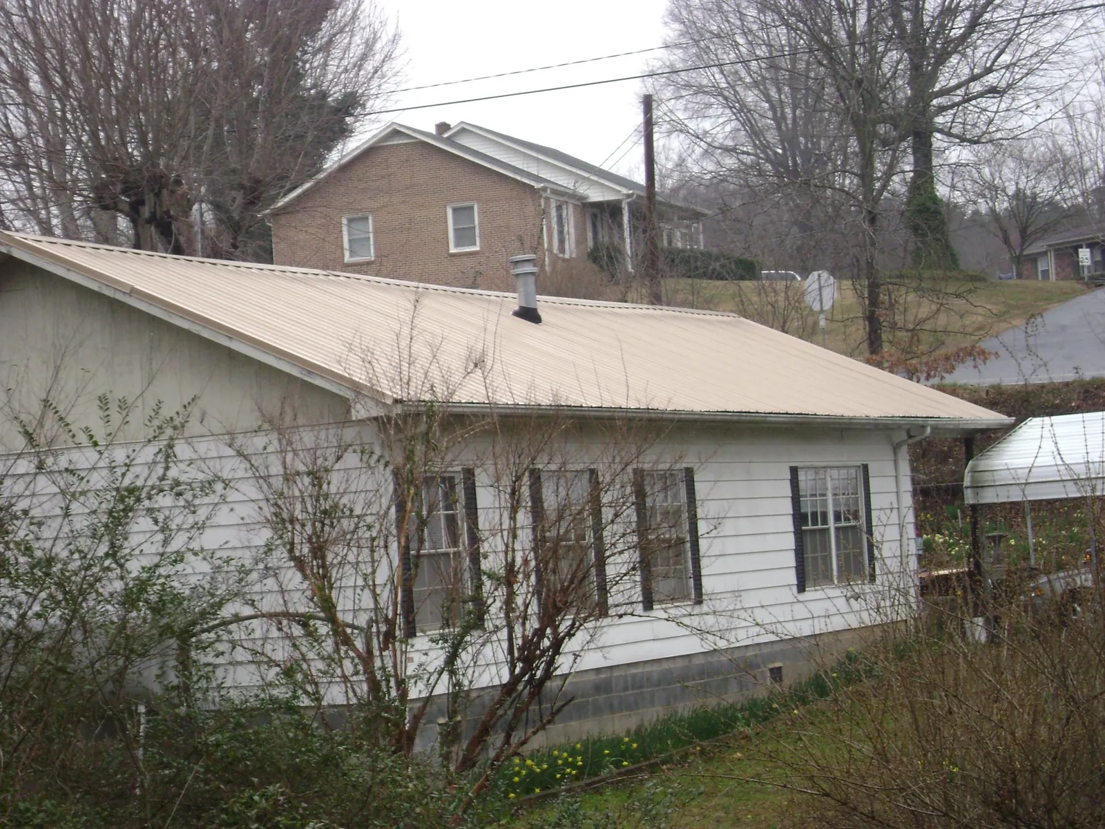 Tan metal roof on a white sided house set into a hillside — Commercial Roofing by Roofing Brothers in Boxborough